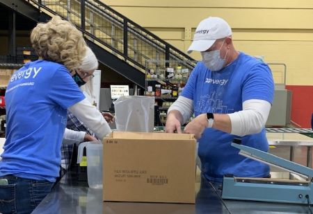Two Evergy volunteers in blue shirts pack a box of food items for distribution