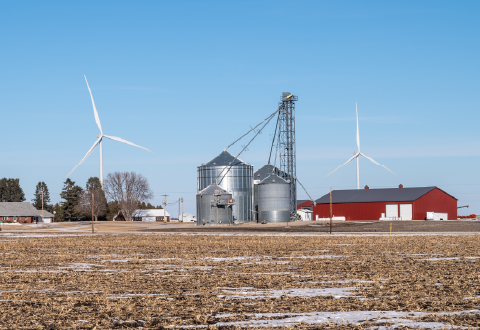 A family farm with grain silos, a red barn and wind turbines